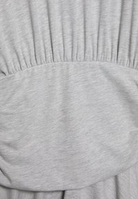 Svetlo siva tkanina z nabranim elastičnim detajlom in gladko ovalno obližem, prišitimi na sredino.