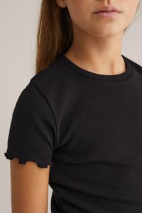 Melna ribota T-krekla ar īsām piedurknēm un viļņotu apakšmalu. Gluda tekstūra un pieguļoša forma izceļ apģērba vienkāršību un daudzpusību.