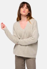 V-Ausschnitt, oversized, hellbeige Pullover aus weichem, strukturiertem Stoff; verfügt über gerippte Bündchen und einen gerippten Saum, kombiniert mit braunen gemusterten Hosen.