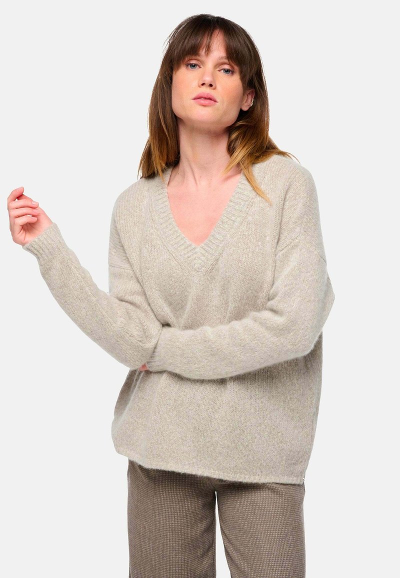 V-Ausschnitt, oversized, hellbeige Pullover aus weichem, strukturiertem Stoff; verfügt über gerippte Bündchen und einen gerippten Saum, kombiniert mit braunen gemusterten Hosen.