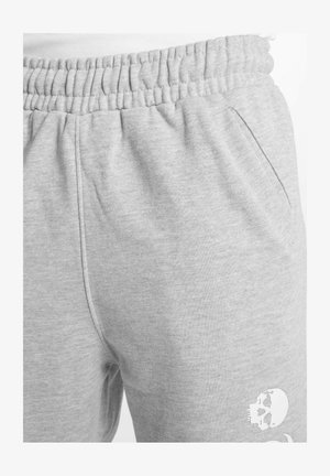 Pelēki sporta bikses ar elastīgu jostu, sānu kabatām un balto mirstīgo galvaskausa grafiku uz apakšstilba, izgatavotas no mīksta kokvilnas materiāla.