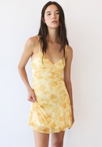 Gelbes Blumenkleid mit dünnen Trägern und V-Ausschnitt, aus weichem, fließendem Stoff mit einem ausgestellten Saum.