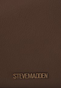 Brūna teksturēta mākslīgā āda maks ar iegravētu zelta "STEVE MADDEN" logotipu apakšā. Vienkārša, taisnstūra forma bez papildu akcentiem.