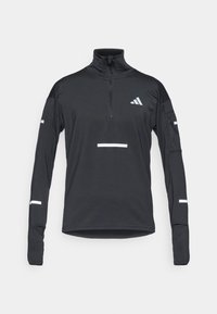 Melnā sporta krekls ar augstu apkakli un ceturtdaļas rāvējslēdzēju. Iekļauj baltas atstarojošas detaļas un teksturētu audumu. Garas piedurknes ar iestrādātiem pirkstu caurumiem.