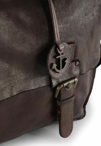 Bolso de cuero marrón con una superficie texturizada, que presenta un logo de ancla, hebilla de metal y detalles de costura en contraste.