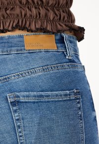 Modré džíny z denimu s hnědou koženou nášivkou s nápisem "Vero Moda" na zadním pasu a podrobným prošíváním na kapsách.