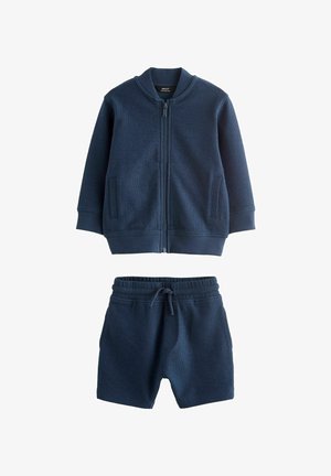 Set din jachetă și pantaloni scurți de culoare bleumarin, realizat dintr-un material texturat. Jacheta are un fermoar în față și două buzunare laterale; pantalonii scurți au un braț elastic la talie.