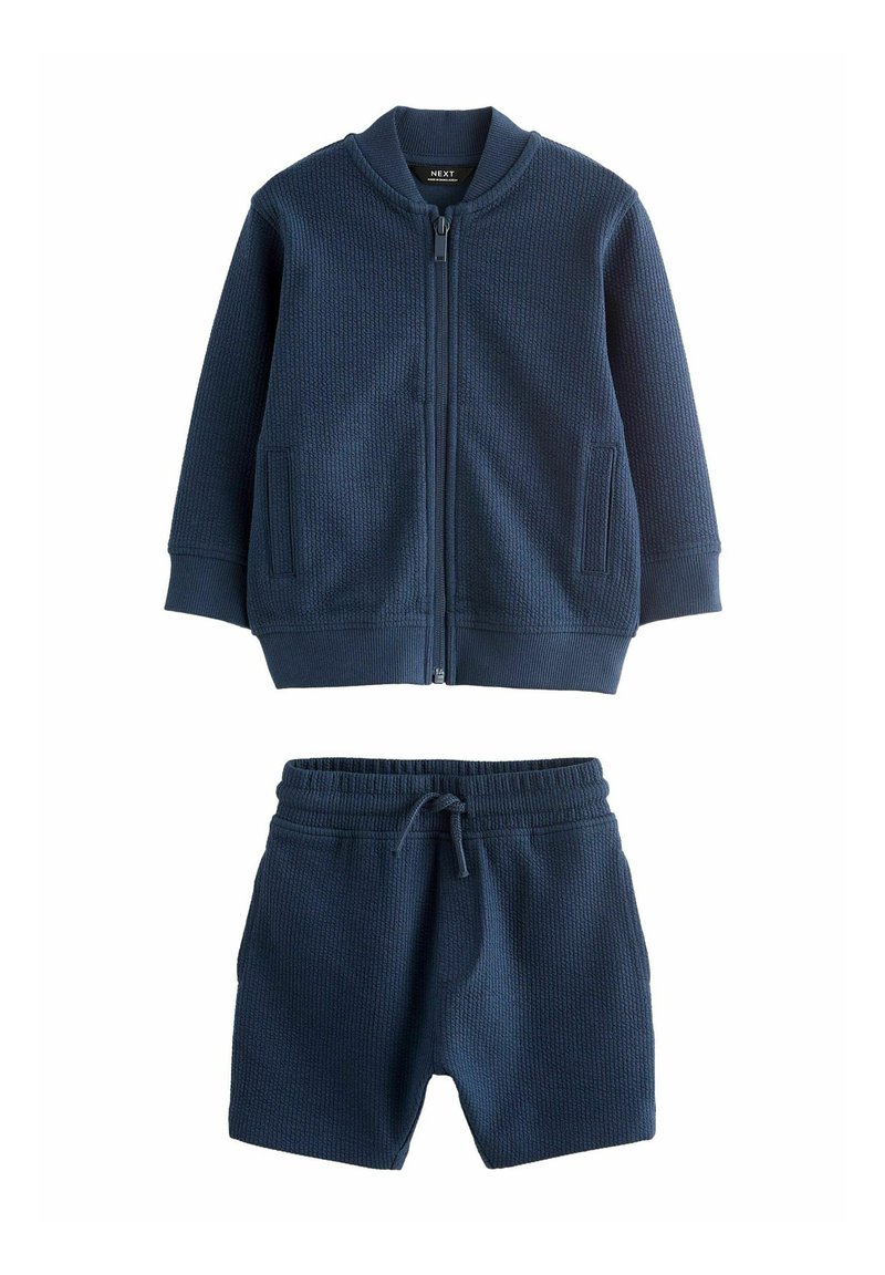 Marineblå jacka och shorts-set i strukturerad tyg. Jackan har dragkedja fram och två sidofickor; shortsen har resårmidja.