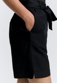 Shorts noirs en tissu léger, dotés d'une taille à nouer, de poches latérales et d'une coupe légèrement ample avec des fentes à l'ourlet.