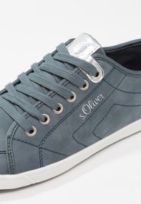 Grå vardagssneaker med en slät textur, silverfärgade öglor och vit sula. Har dekorativ sömnad och logotyp på sidan.