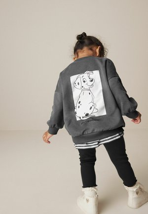 Pilkas megztinis su animaciniu dalmatinu piešiniu ant nugaros, juodos legginsės ir baltos batai su nėrinių akcentais. Atsipalaidavęs kirpimas ir minkšta tekstūra.