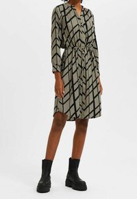 Robe à motif noir et crème avec des manches longues, un col et une taille à cordon ; associée à des bottines noires épaisses.