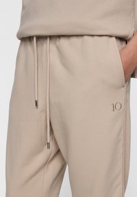 Beige sweatpants van zachte stof, met een elastische tailleband met trekkoord, zijzakken en geborduurde "10"-detail.