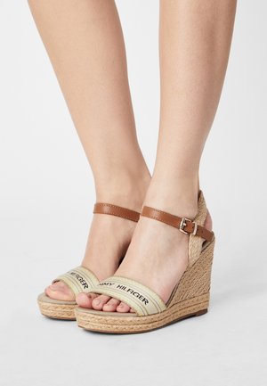 Sandales compensées avec une sangle de cheville en cuir marron et une bande en tissu léger arborant le texte de la marque. Talon compensé en jute naturel.