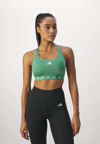 Soutien-gorge de sport vert avec logo Adidas blanc et bande à motifs, associé à un legging noir taille haute avec un petit logo blanc.