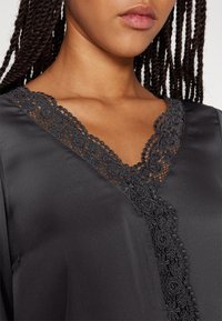 Vêtement en satin noir avec un décolleté en V orné de détails en dentelle sophistiqués. Texture lisse avec de délicates bordures en dentelle florale le long des bords.