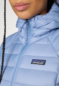 Krupanja osobe koja nosi svijetloplavu Patagonia jaknu s puhovim punjenjem i zatvaračem na ovratniku, a vidi se i pletena pletenica.