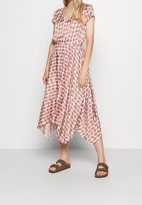 Vloeiende jurk met een v-hals, korte mouwen, rood-wit loofpatroon, cinched taille, asymmetrische zoom, gecombineerd met bruine sandalen.