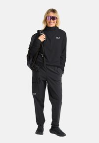 Zwarte outdoor kleding met een ritssluiting tot op de kwartlengte en elastische broek. Inclusief een rugzak en reflecterende zonnebril.