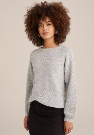 Maglione grigio a maglia con un motivo a zig zag, scollatura rotonda e maniche lunghe. Realizzato in un morbido tessuto testurizzato, abbinato a una gonna scura.
