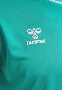 Turkos träningsskjorta i slitstarkt tyg, med en vit "hummel"-logotyp och en karakteristisk bi-design, samt rund halsringning.