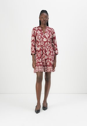Red patterned dress with a V-neck, three-quarter sleeves, and a gathered waist. The fabric features intricate white designs and a ruffled hem.
