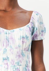 Rochie florală compusă dintr-un material alb cu modele albastre și purpurii, cu decolteu pătrat și mâneci bufante cu manșete elastice și talie smockată.