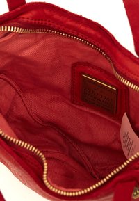 Interno di una borsa a tracolla in pelle rossa con una texture liscia, dotata di una cerniera in tono oro, etichetta del marchio e rivestimento in tessuto.