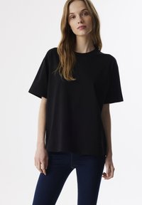 Zwarte katoenen t-shirt met korte mouwen, ronde hals, ontspannen pasvorm, gladde textuur en geen zichtbare patronen of logo's. Draagt met donkerblauwe jeans.