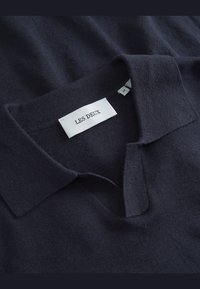 Marineblå polo skjorte laget av myk stoff med krage, med et merke merket "LES DEUX" og størrelse "M."