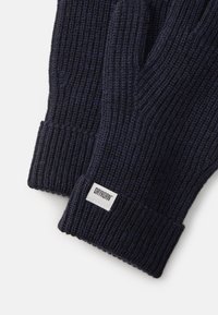 Guanti lavorati a maglia blu navy con una texture a coste e un polsino ripiegato; presenta una piccola etichetta bianca con il logo "DRYKORN".