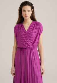 Rochie din satin fucsia cu pliseuri verticale, decolteu în V și mâneci scurte. Designul fluid se strânge în talie, evidențiind silueta.