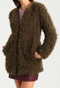 Brązowy, puszysty, oversize kardigan o textured powierzchni, z otwartym przodem i dwoma bocznymi kieszeniami. W zestawie ze dopasowanym topem i spódnicą.