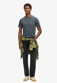 Grå kortærmet t-shirt, sorte jeans, grønternet skjorte bundet om livet, og cremefarvede sneakers. Simpelt design, afslappet stof og farver.