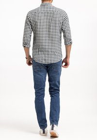 Czarna i biała koszula w kratę z długimi rękawami, dżinsy i białe trampki, prezentujące casualowy widok z tyłu.