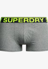 Boxers de algodón gris con una cinturilla negra que presenta letras amarillas brillantes de "SUPERDRY". Textura suave, ajuste ceñido, diseño práctico.