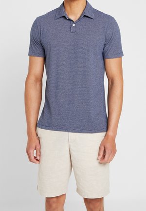 Mørkeblå stribet polo-shirt med en knappet krave, båret med lysebeige shorts. Har korte ærmer og en afslappet pasform.