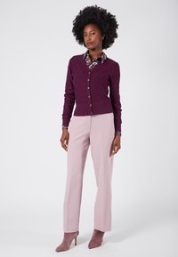 Lila stickad kofta med diamantmönster, knappstängning, kombinerad med ljusrosa byxor och matchande mocka klackar.