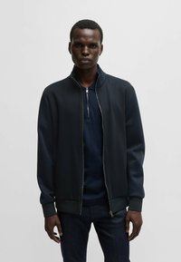 Sweatshirt jacket in dark navy, made from smooth, textured fabric. Features a stand-up collar and zip closure, with ribbed cuffs and hem.