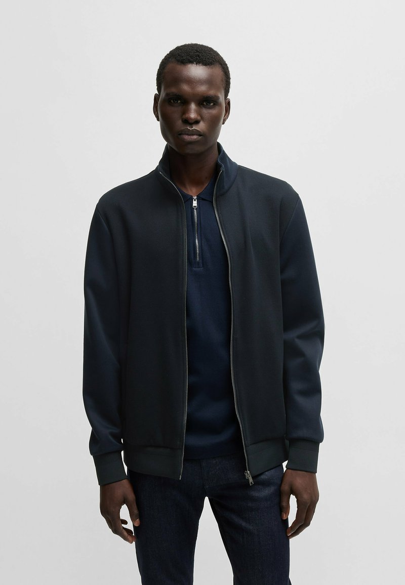 Sweatshirt jacket in dark navy, made from smooth, textured fabric. Features a stand-up collar and zip closure, with ribbed cuffs and hem.