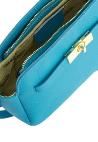 Blaues strukturiertes Lederhandtasche mit goldener Reißverschluss und Verschluss. Das Innere verfügt über ein beiges Futter mit einem Logomuster und einer zusätzlichen Tasche.
