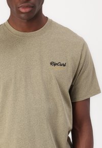 T-shirt in cotone verde oliva con maniche corte, caratterizzato da un logo "RipCurl" nero e oro stampato sull'area sinistra del petto.