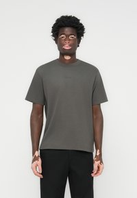 Kurzärmliges T-Shirt mit Rundhalsausschnitt aus dunklem grauen Baumwollstoff in entspannter Passform. Mit minimalem Branding auf der Brust.