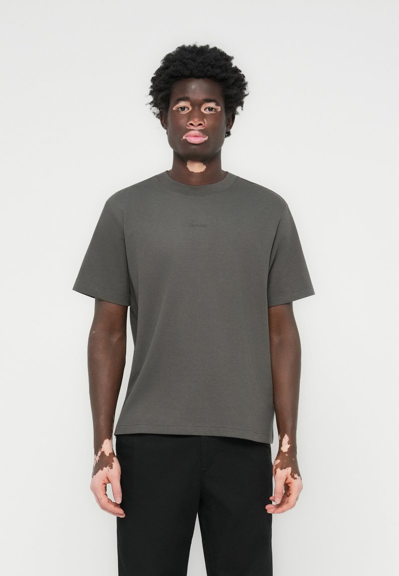 Kurzärmliges T-Shirt mit Rundhalsausschnitt aus dunklem grauen Baumwollstoff in entspannter Passform. Mit minimalem Branding auf der Brust.