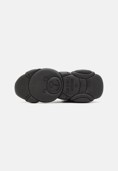 Black rubber shoe sole featuring a teddy bear design with textured patterns and the phrase "THIS IS NOT A MOSCHINO TOY" embossed.