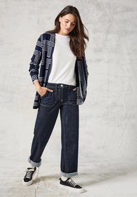 Mörkblå och vit mönstrad cardigan, vit t-shirt och mörk denimvidbyxor. Outfit avslutad med svarta sneakers och uppvikta fållar.