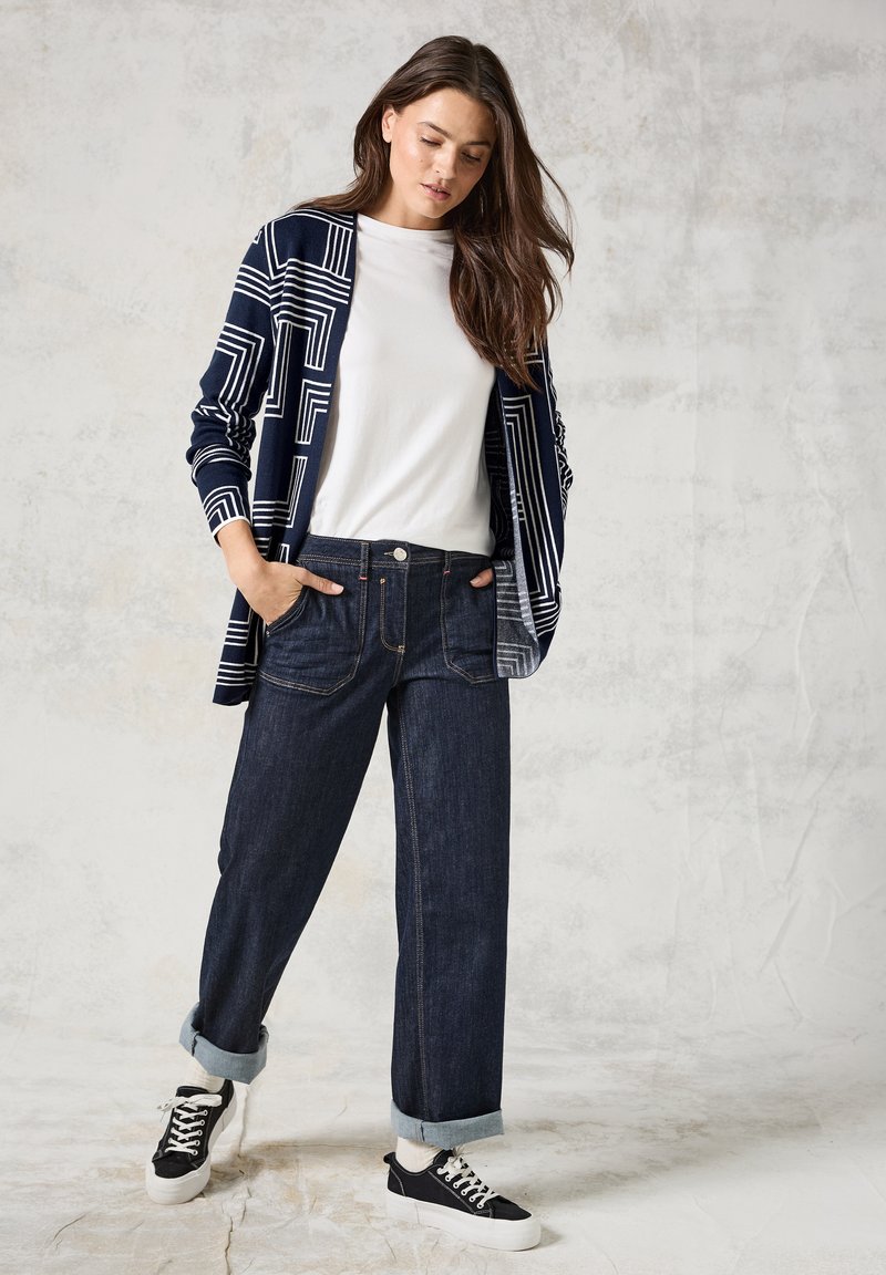 Mörkblå och vit mönstrad cardigan, vit t-shirt och mörk denimvidbyxor. Outfit avslutad med svarta sneakers och uppvikta fållar.