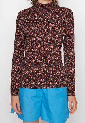 Person wearing a long-sleeve, high-neck floral top with red, pink, and orange flowers, paired with bright blue shorts.