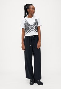 Top corto bianco con dettagli in pizzo nero, abbinato a pantaloni neri larghi e stivali neri chunky, con coulisse e accenti argentati.