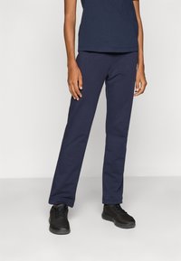 Marine joggebukser laget av mykt stoff, med en komfortabel passform og elastisk midjebånd, kombinert med svarte treningssko.